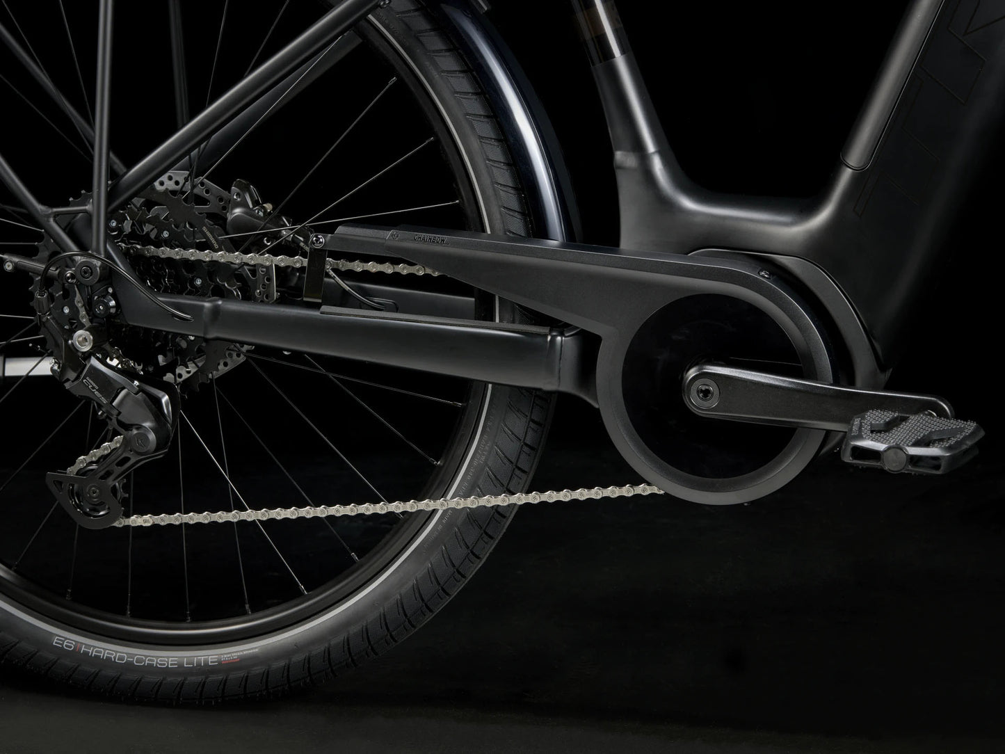 Side detail view of the drivetrain of the Trek Verve+ 3 Lowstep Gen 3 e-Bike in Black, shown on a black background. It includes fenders, lights, rear rack, suspension seatpost, and kickstand.