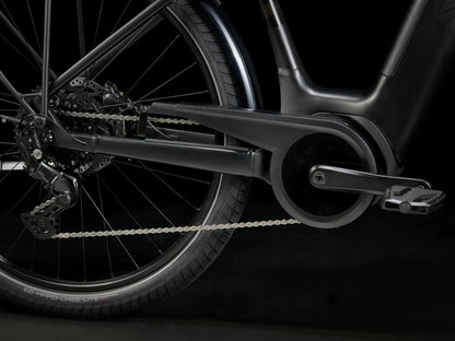 Side detail view of the drivetrain of the Trek Verve+ 3 Lowstep Gen 3 e-Bike in Black, shown on a black background. It includes fenders, lights, rear rack, suspension seatpost, and kickstand.