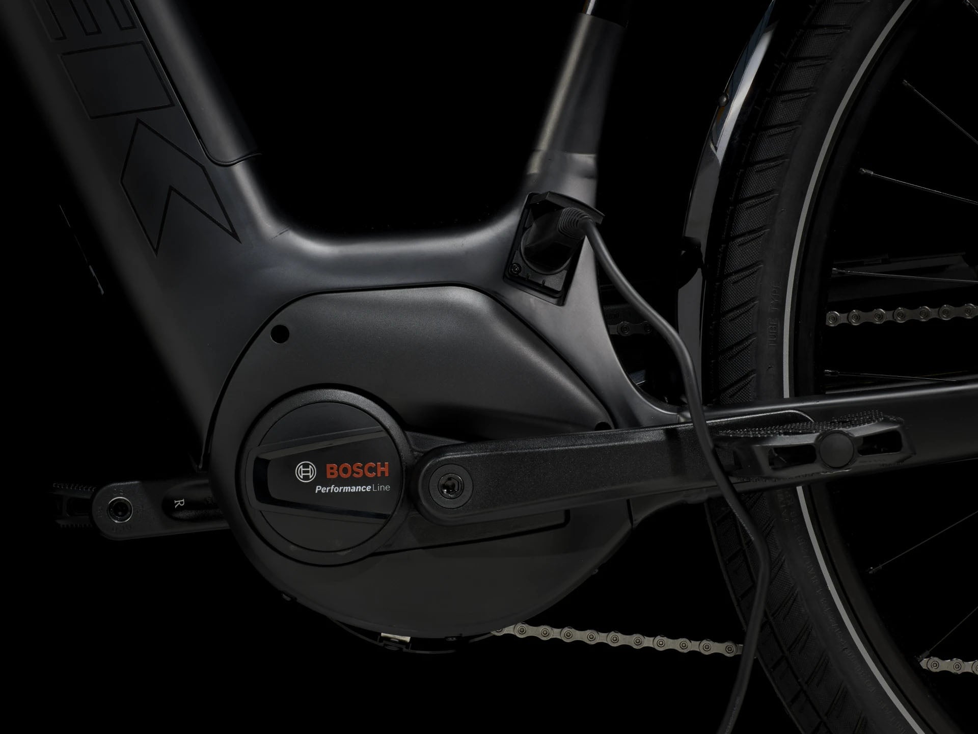 Side detail view of the Bosch motor on the Trek Verve+ 3 Lowstep Gen 3 e-Bike in Black, shown on a black background. It includes fenders, lights, rear rack, suspension seatpost, and kickstand.
