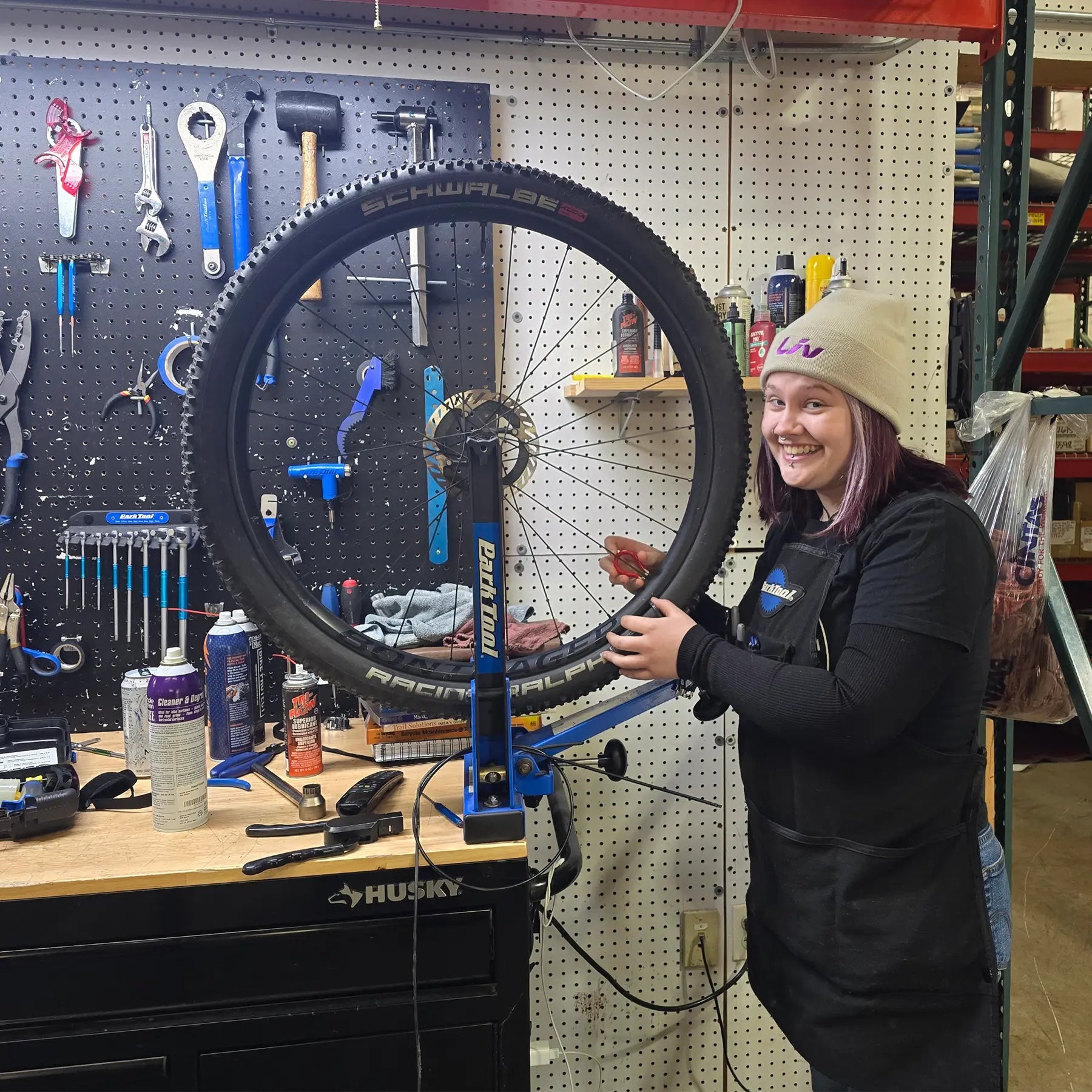 Person working on a bicycle wheel in a workshop with tools and equipment on the wall.