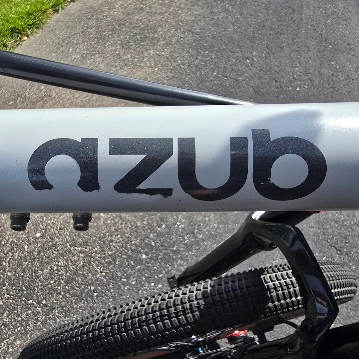 Closeup view of the scuffed Azub logo on the Azub Demo Six Bosch Performance CX Dynamic Grey Recumbent Bike in an outdoor setting.