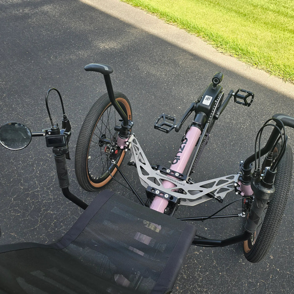 Closeup view of the front suspension, mirror, handlebars and controls on the Azub Demo Ti-Fly 20 Enviolo Shimano EP6 Pastel Violet Recumbent Trike in an outdoor setting.