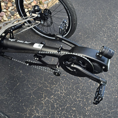 Closeup view of the Shimano motor, headlight and quick adjust on the Azub Demo Ti-Fly 26 Shimano EP6 Deep Black Recumbent Trike in an outdoor setting.