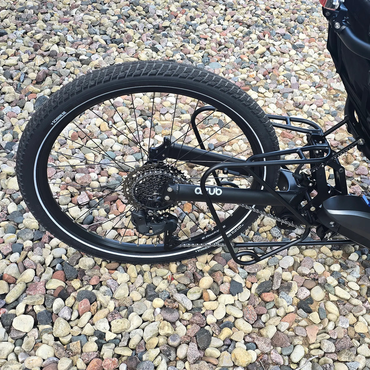 Closeup view of the mid rack, rear wheel, cassette and rear dearailleur on the Azub Demo Ti-Fly 26 Shimano EP6 Deep Black Recumbent Trike in an outdoor setting.
