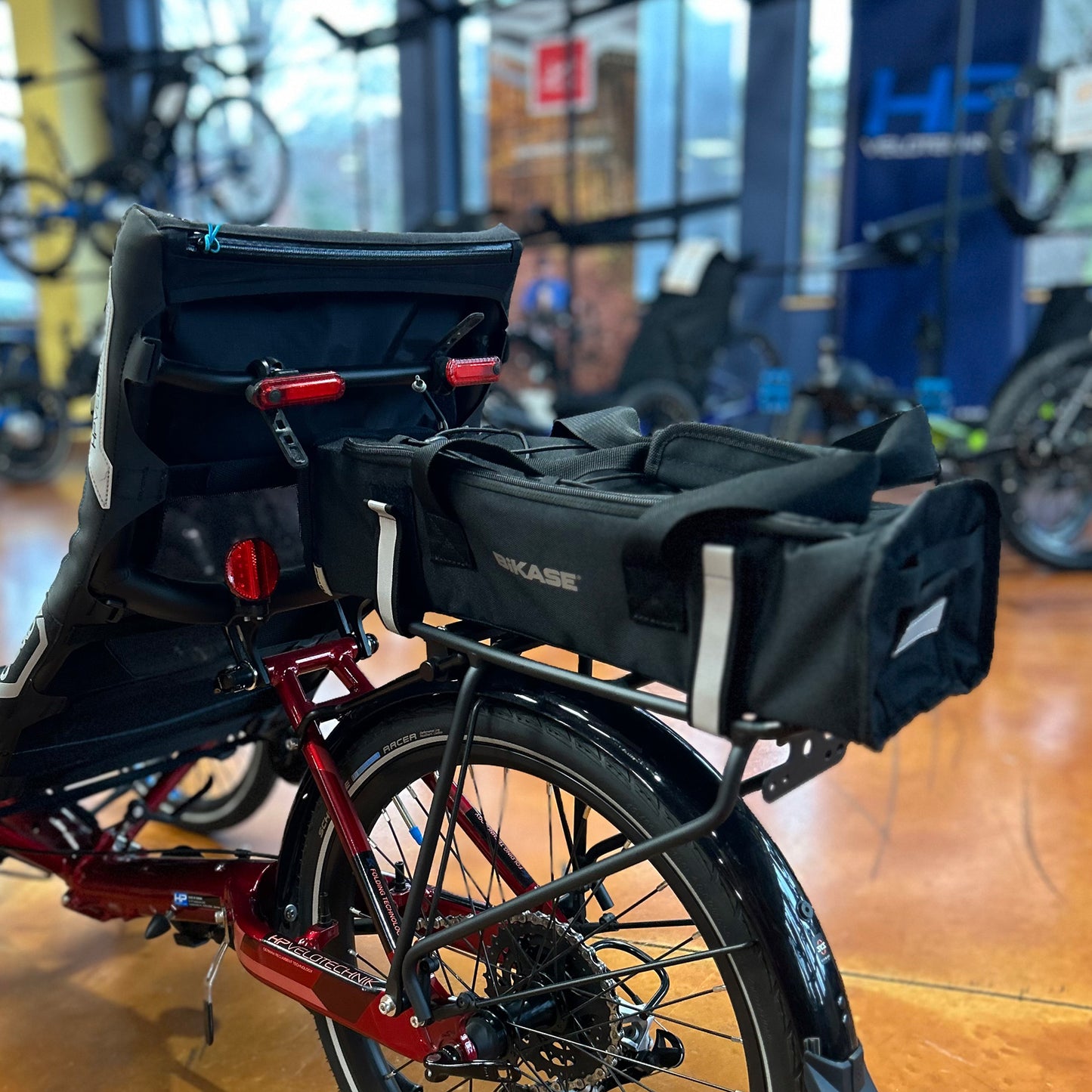 Black battery bag with "BiKASE" branding in reflective silver with a handle and reflective Velcro rack straps on a recumbent trike rack.