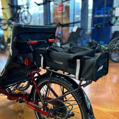 Black battery bag with "BiKASE" branding in reflective silver with a handle and reflective Velcro rack straps on a recumbent trike rack.