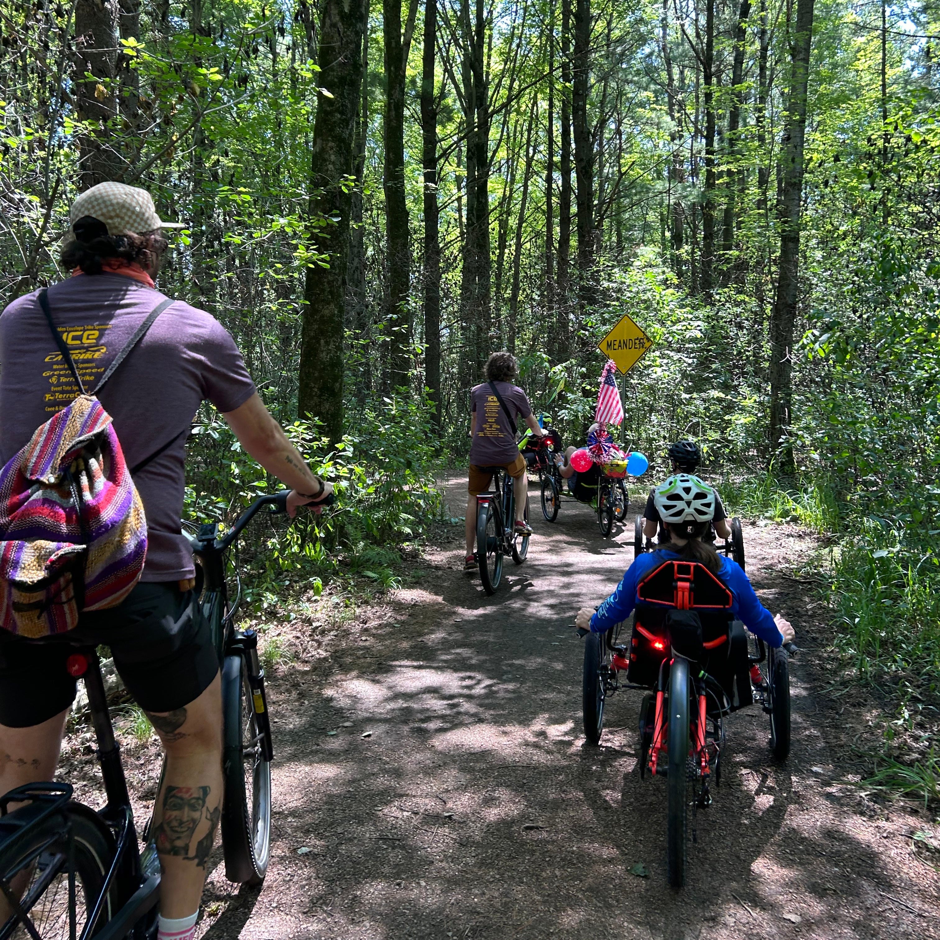 People riding bikes and trike on a gravel path through a forest.
