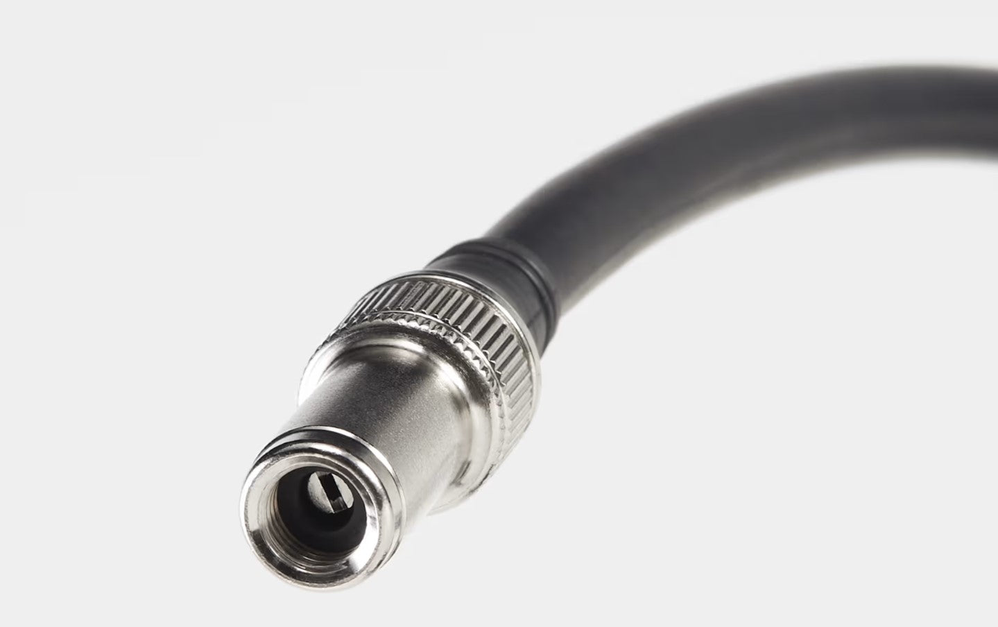 Close up view of silver valve end of the black hose on a Bontrager Digital Shock Pump on a white background. 