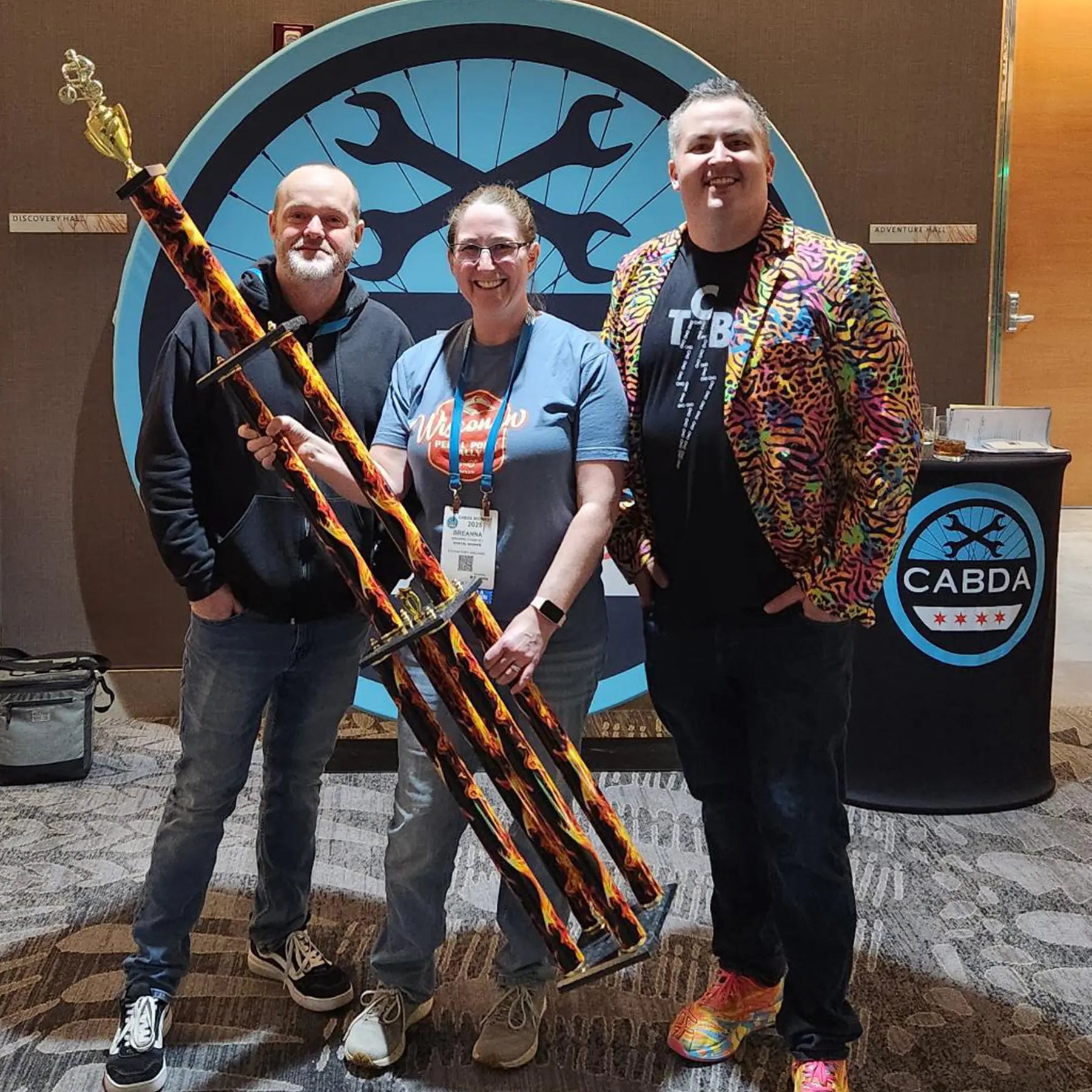 Three people posing with a large decorative trophy in front of a CABDA logo.