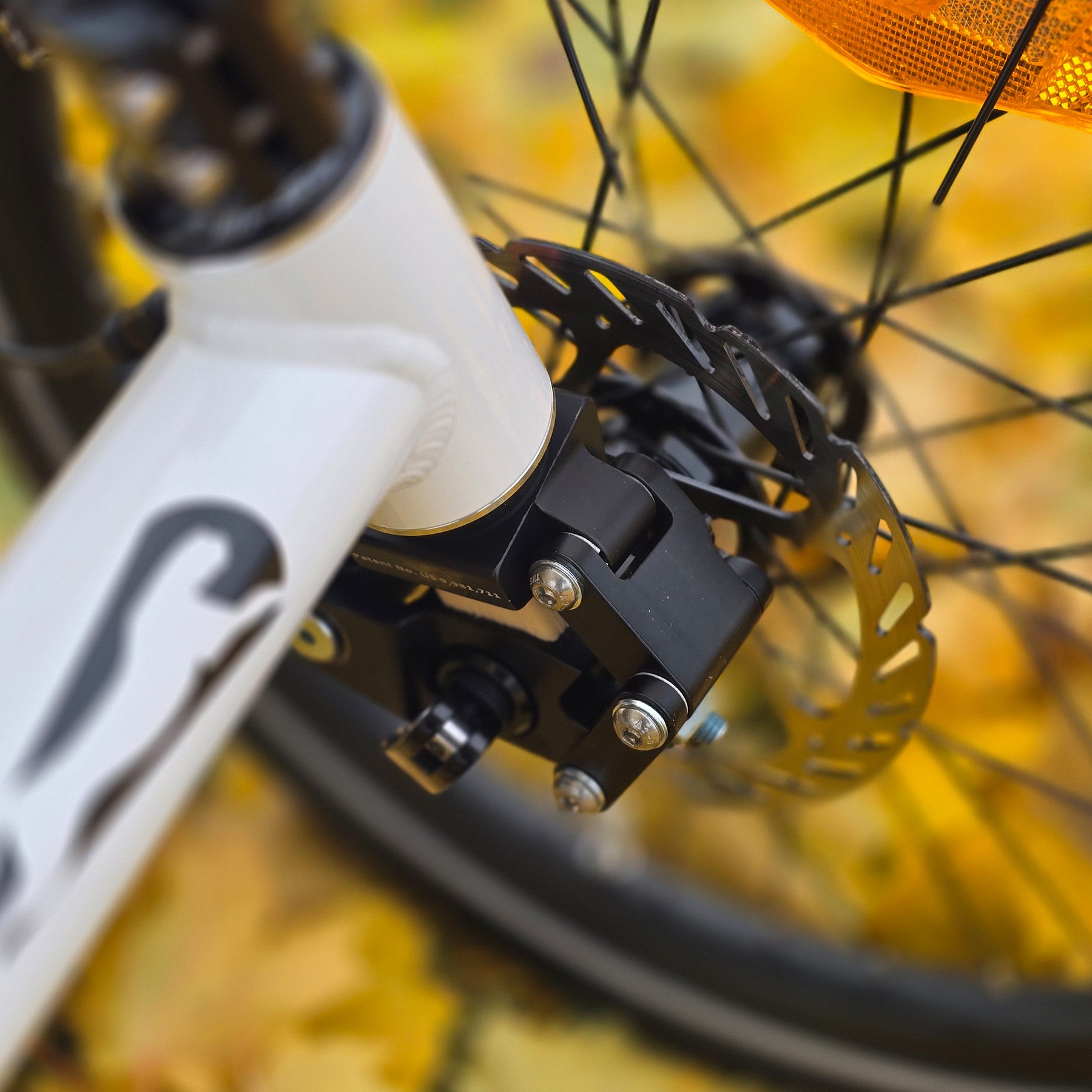 Close-up of a bicycle brake mechanism and front suspension with blurred autumn leaves in the background.