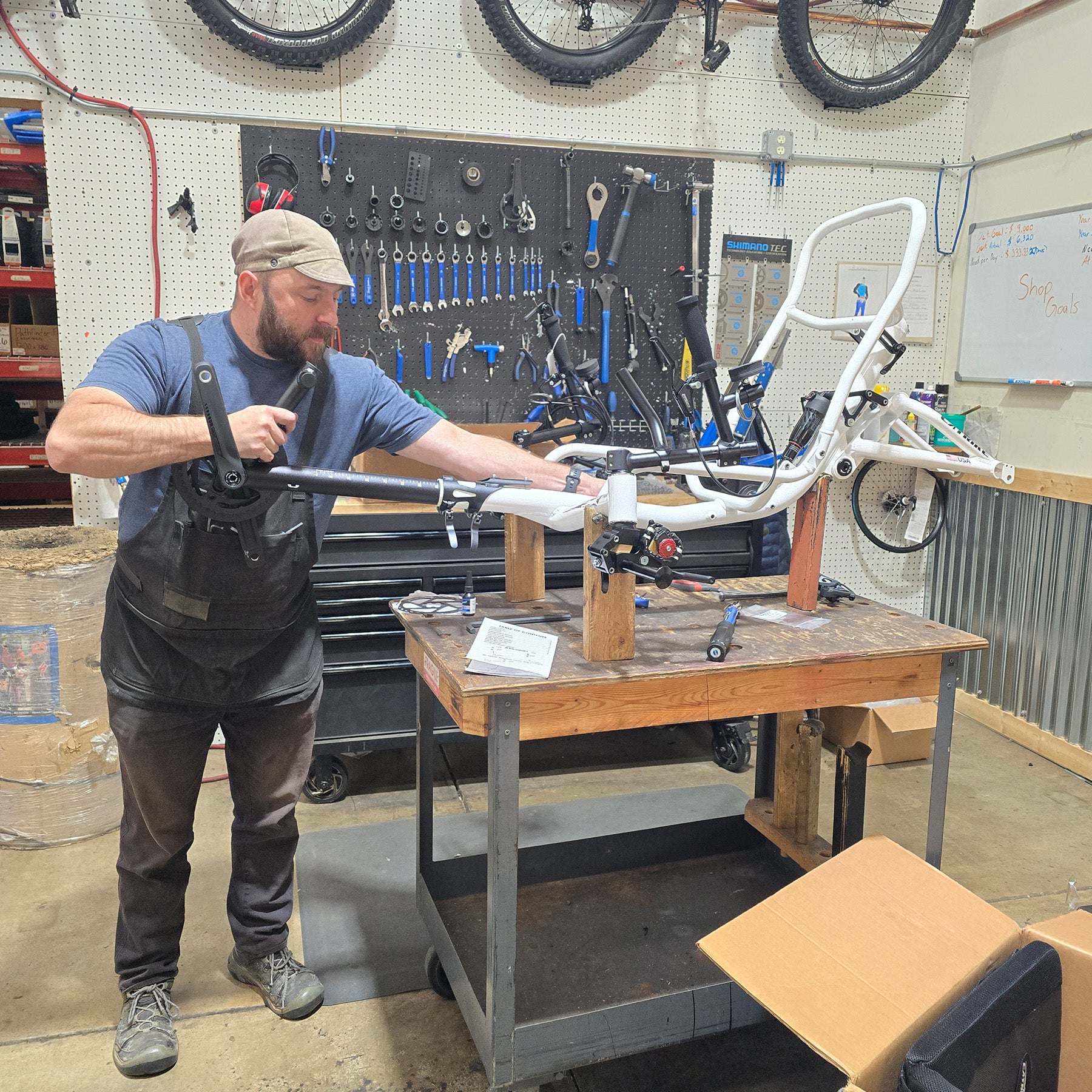 Man working on a tricycle frame in a workshop with tools and equipment around.