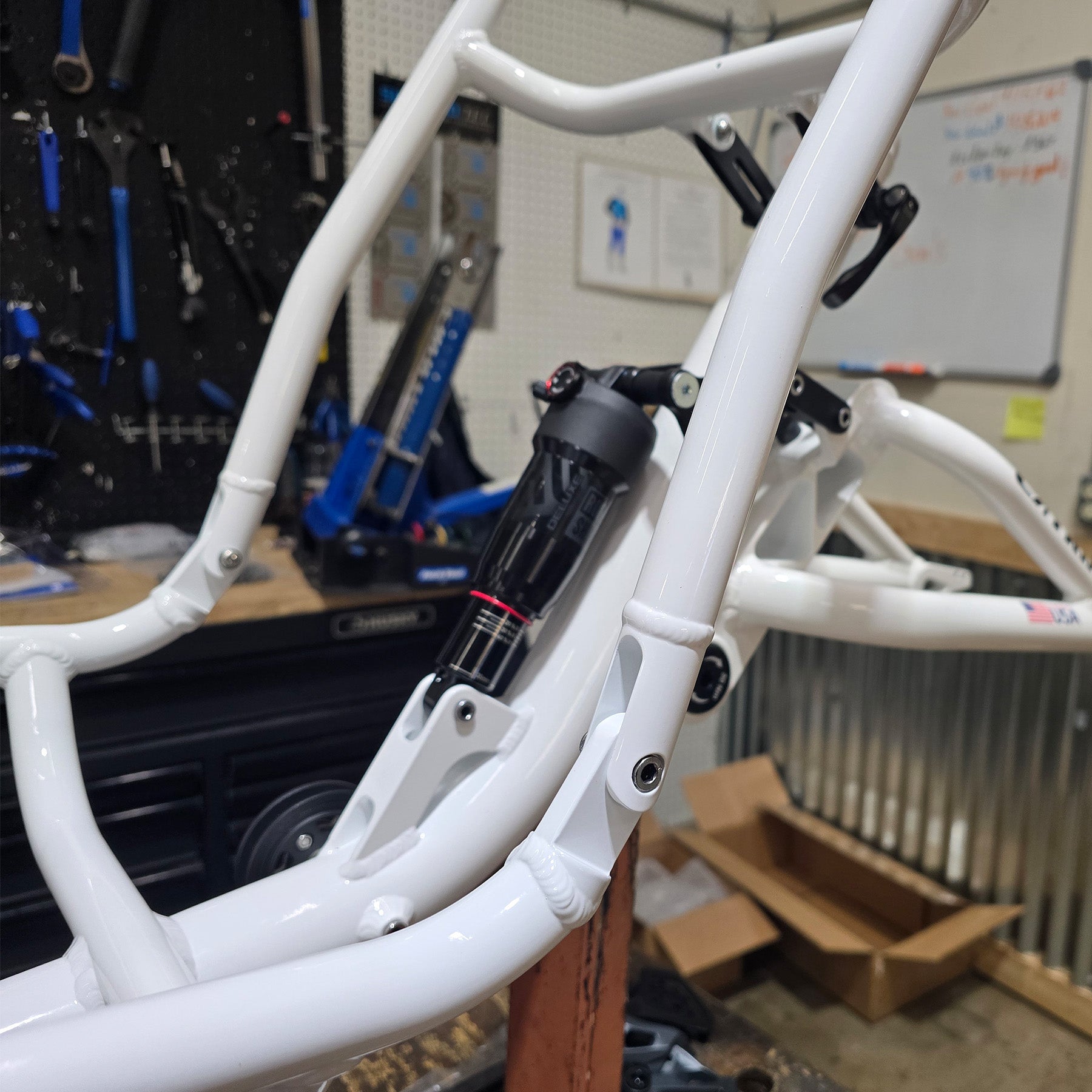White tricycle frame with suspension shock in a workshop setting.