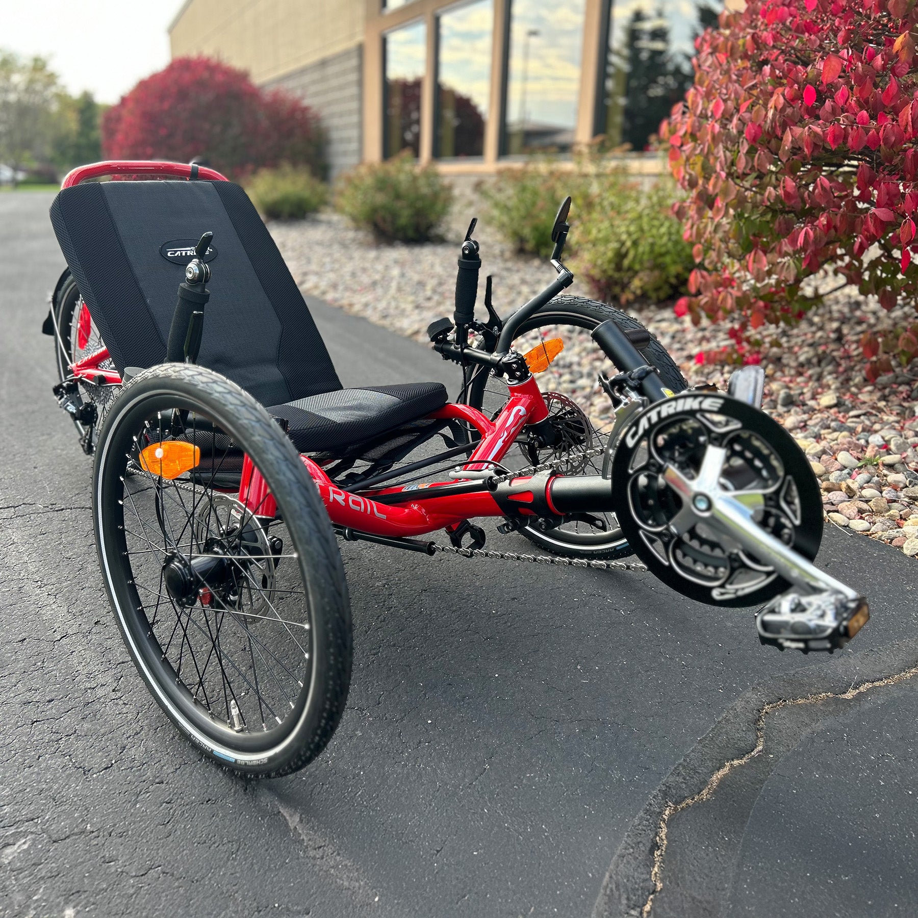Front angled view of a Catrike Trail Compact Recumbent Trike in Lava Red in an outdoor setting.