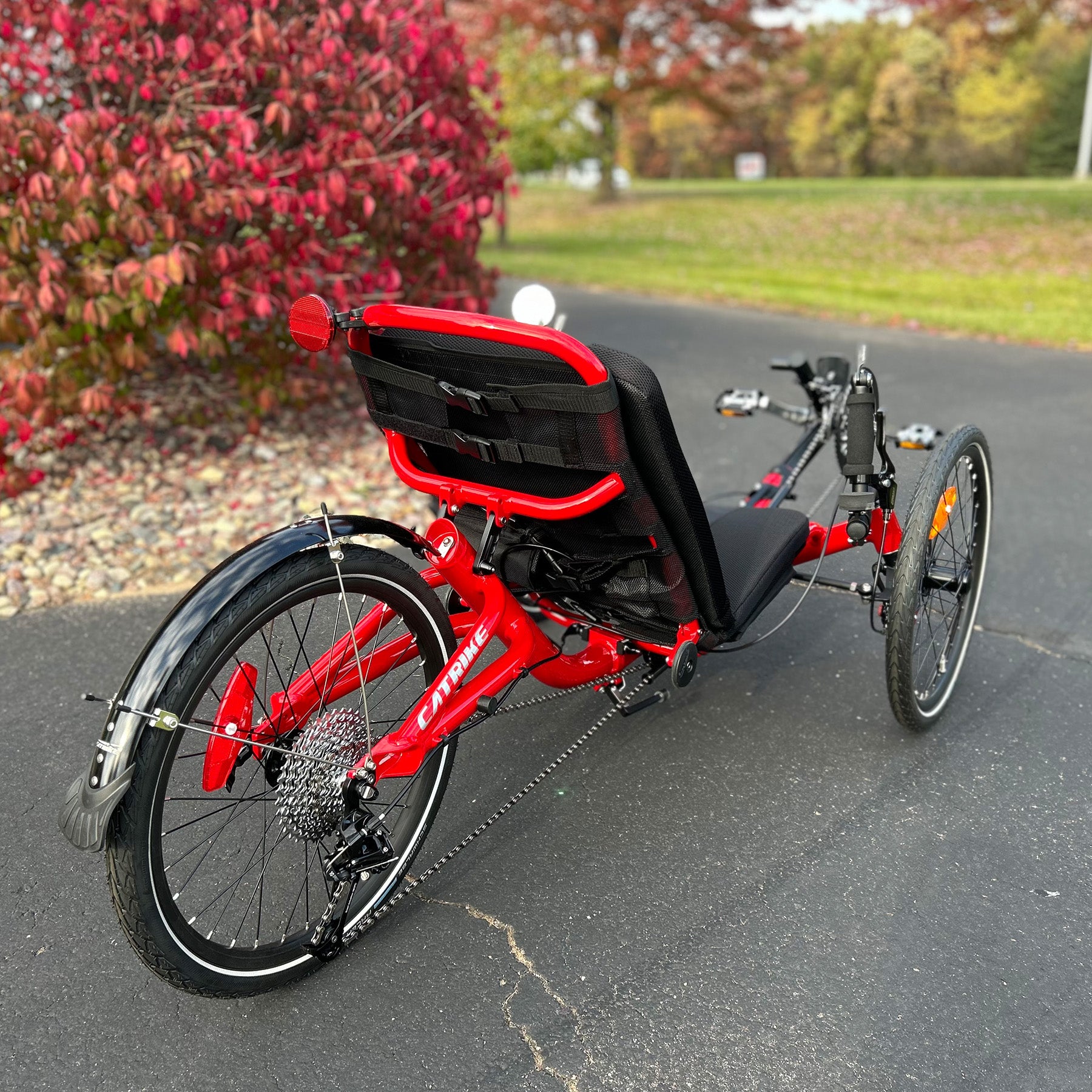 Back angled view of a Catrike Trail Compact Recumbent Trike in Lava Red in an outdoor setting.