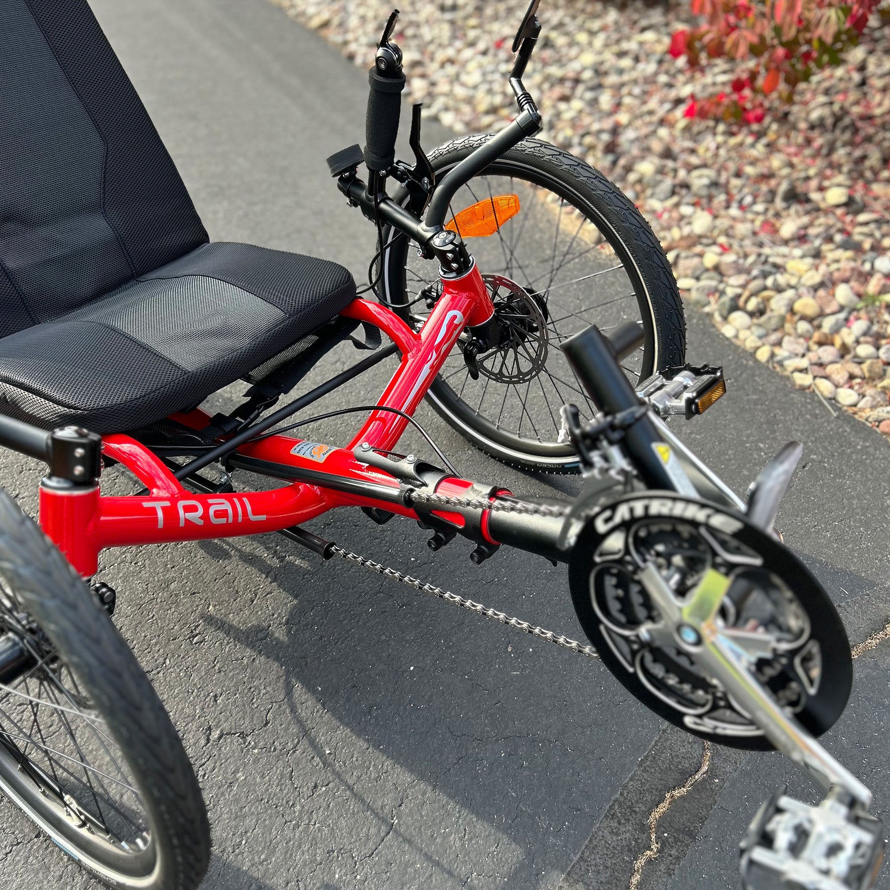 Closeup front view of a Catrike Trail Compact Recumbent Trike in Lava Red in an outdoor setting.