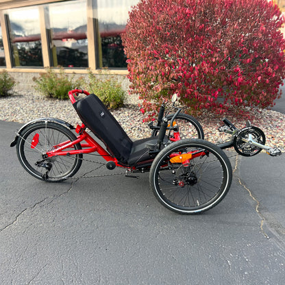 Side view of a Catrike Trail Compact Recumbent Trike in Lava Red in an outdoor setting.