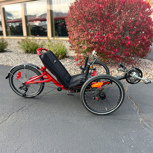 Side view of a Catrike Trail Compact Recumbent Trike in Lava Red in an outdoor setting.
