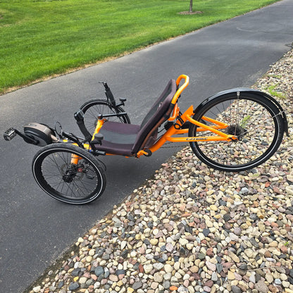Non-drive side view of the Catrike Used 5.5.9. e-Cat Atomic Orange Recumbent Trike in an outdoor setting.
