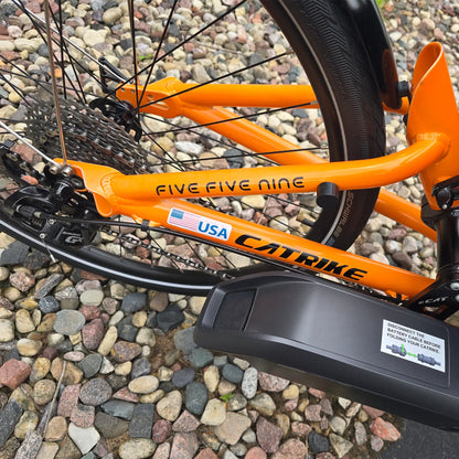 Closeup view of the battery and rear derailleur on the Catrike Used 5.5.9. e-Cat Atomic Orange Recumbent Trike in an outdoor setting.