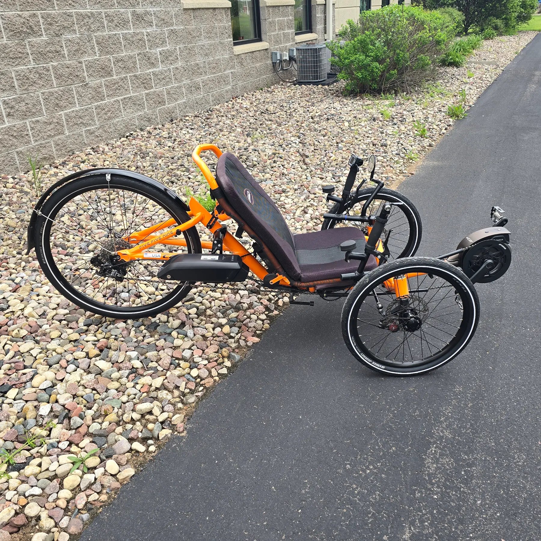 Side view of the Catrike Used 5.5.9. e-Cat Atomic Orange Recumbent Trike in an outdoor setting.