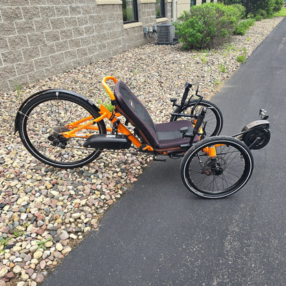 Side view of the Catrike Used 5.5.9. e-Cat Atomic Orange Recumbent Trike in an outdoor setting.