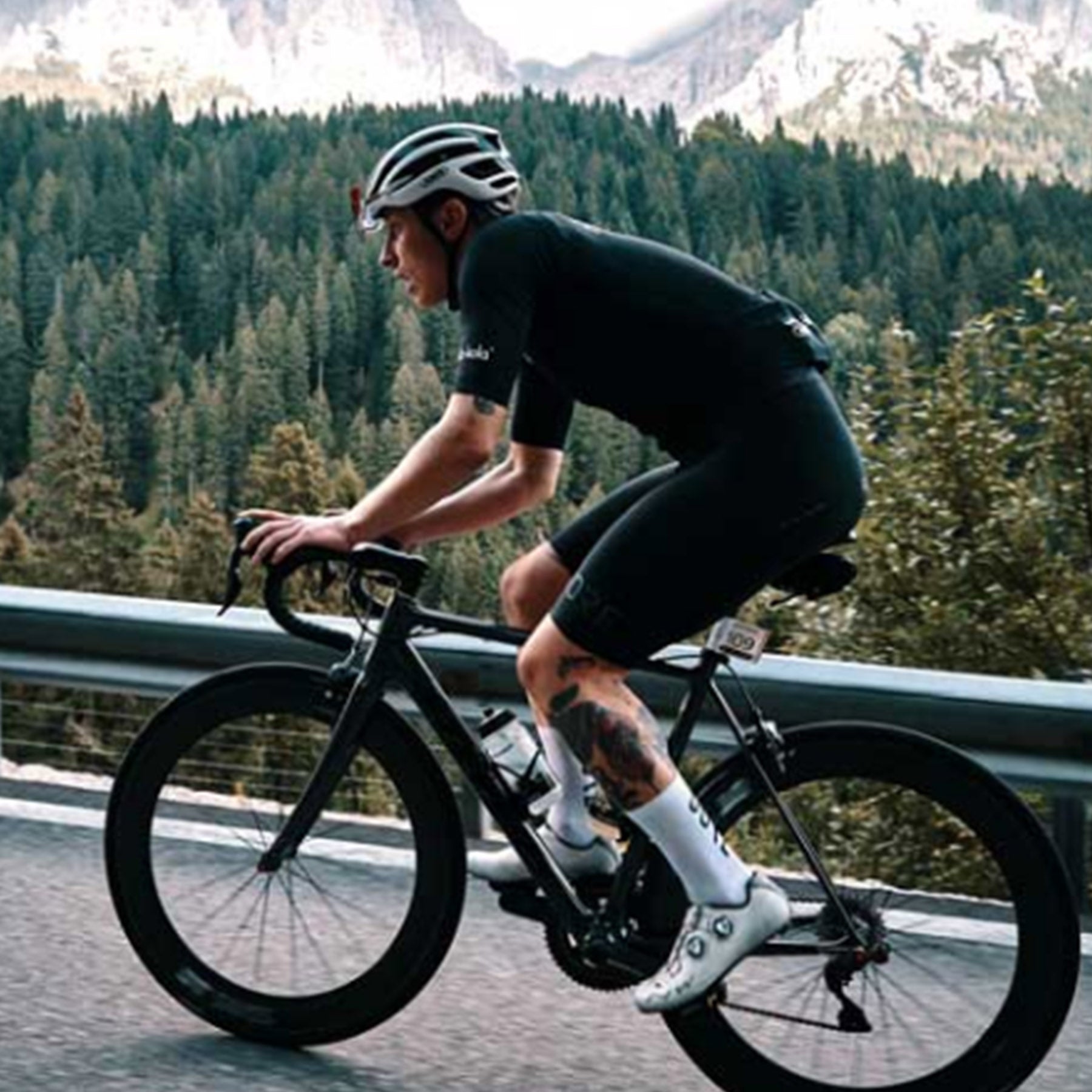 Side view of the Continental Grand Prix 500 S TR Tire in black with white print mounted on a bicycle.  The cyclist riding the bike is riding through the mountains.
