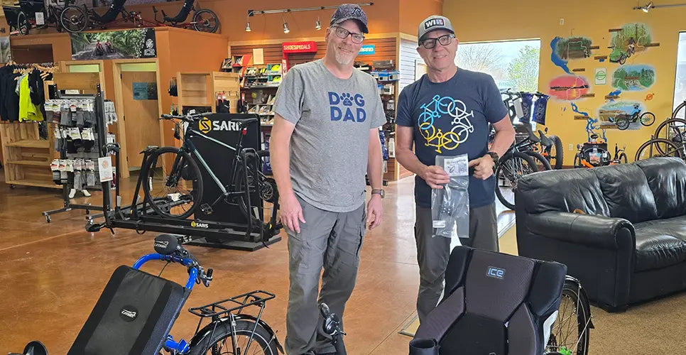 Two men standing in a store with bicycles in the background.