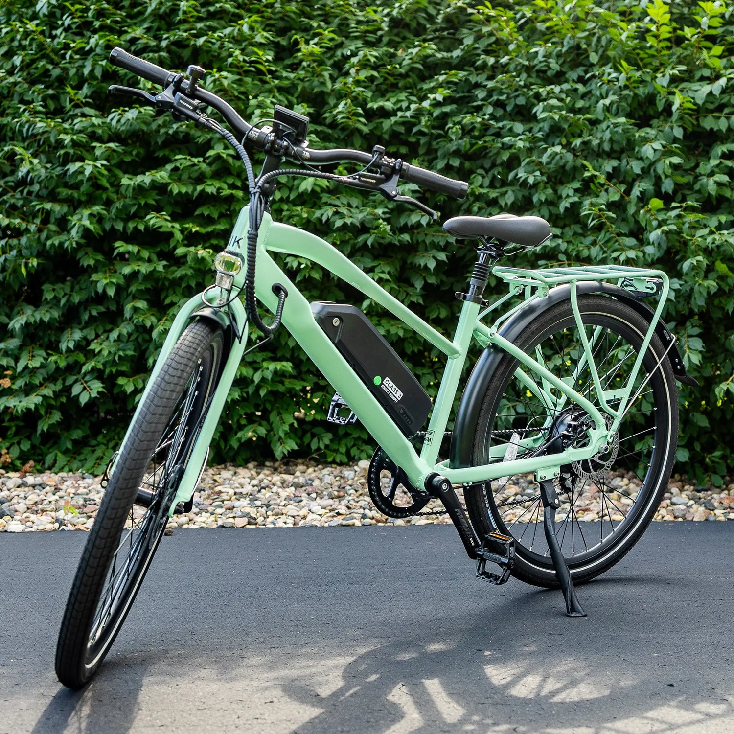 Green electric bicycle parked on a paved surface with greenery in the background