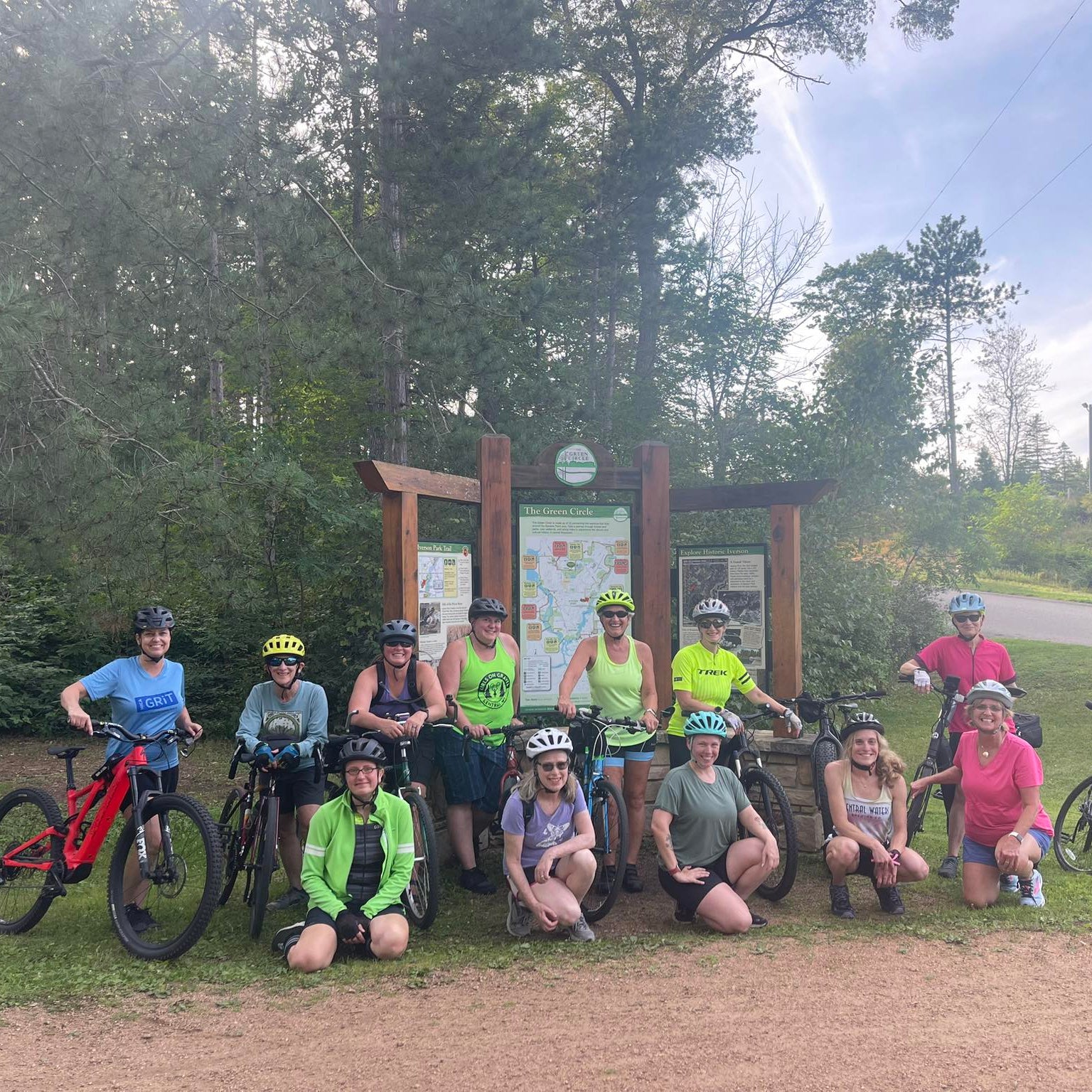 Group of cyclists with their bikes posing for a photo in a park setting on the Green Circle Trail in Stevens Point.