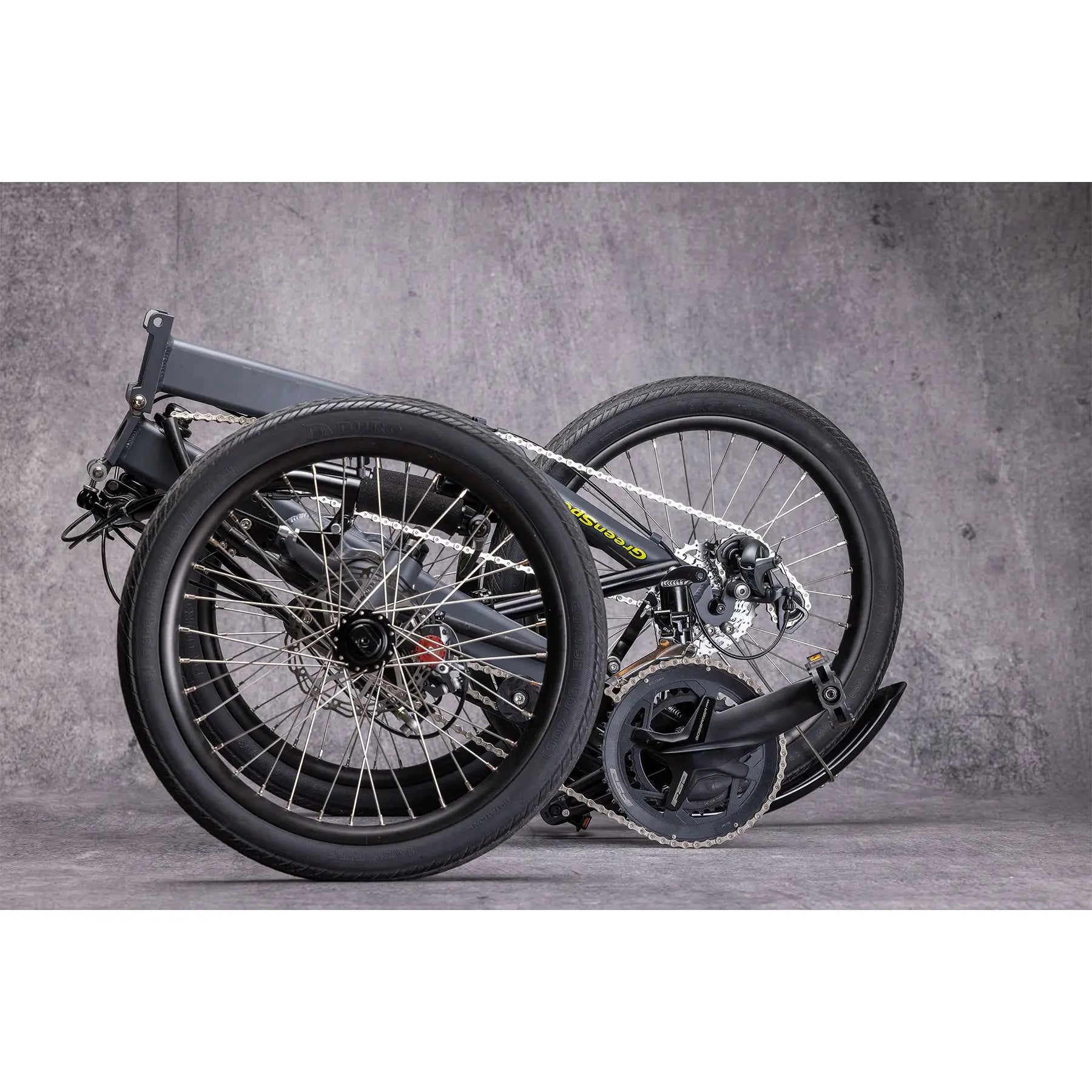 Closeup view of the folded Greenspeed Magnum XL Bosch e-Plus Recumbent Trike in Smoke against a grey background.