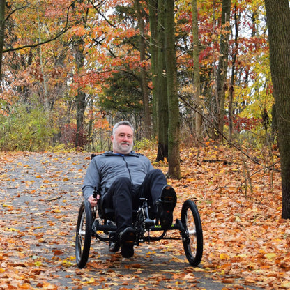 A man rides a Greenspeed Magnum along a bike path during the fall in a forested setting.