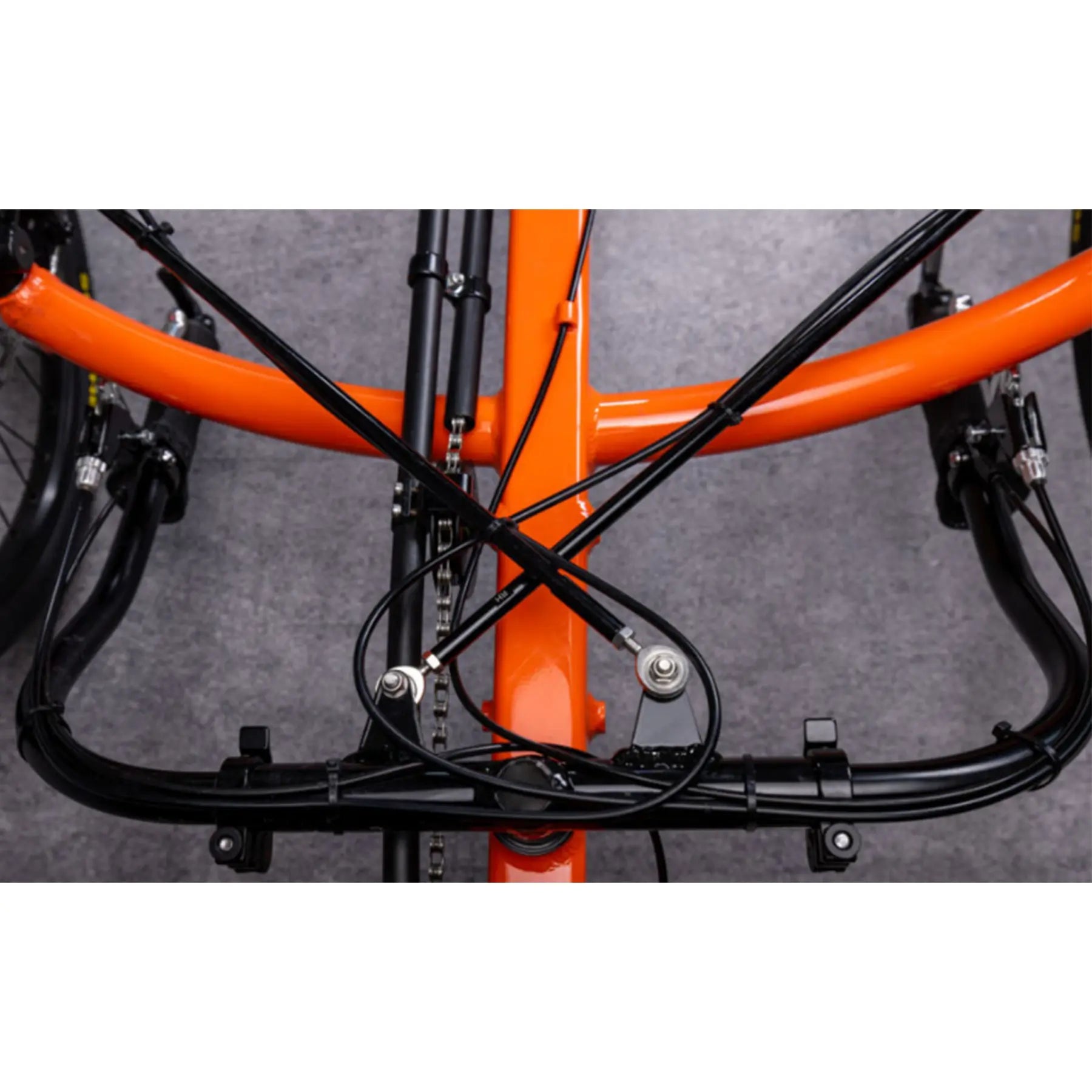 Closeup view of the Greenspeed Magnum XL Recumbent Trike in Tangerine Dream with handlebars folded down against a grey background.