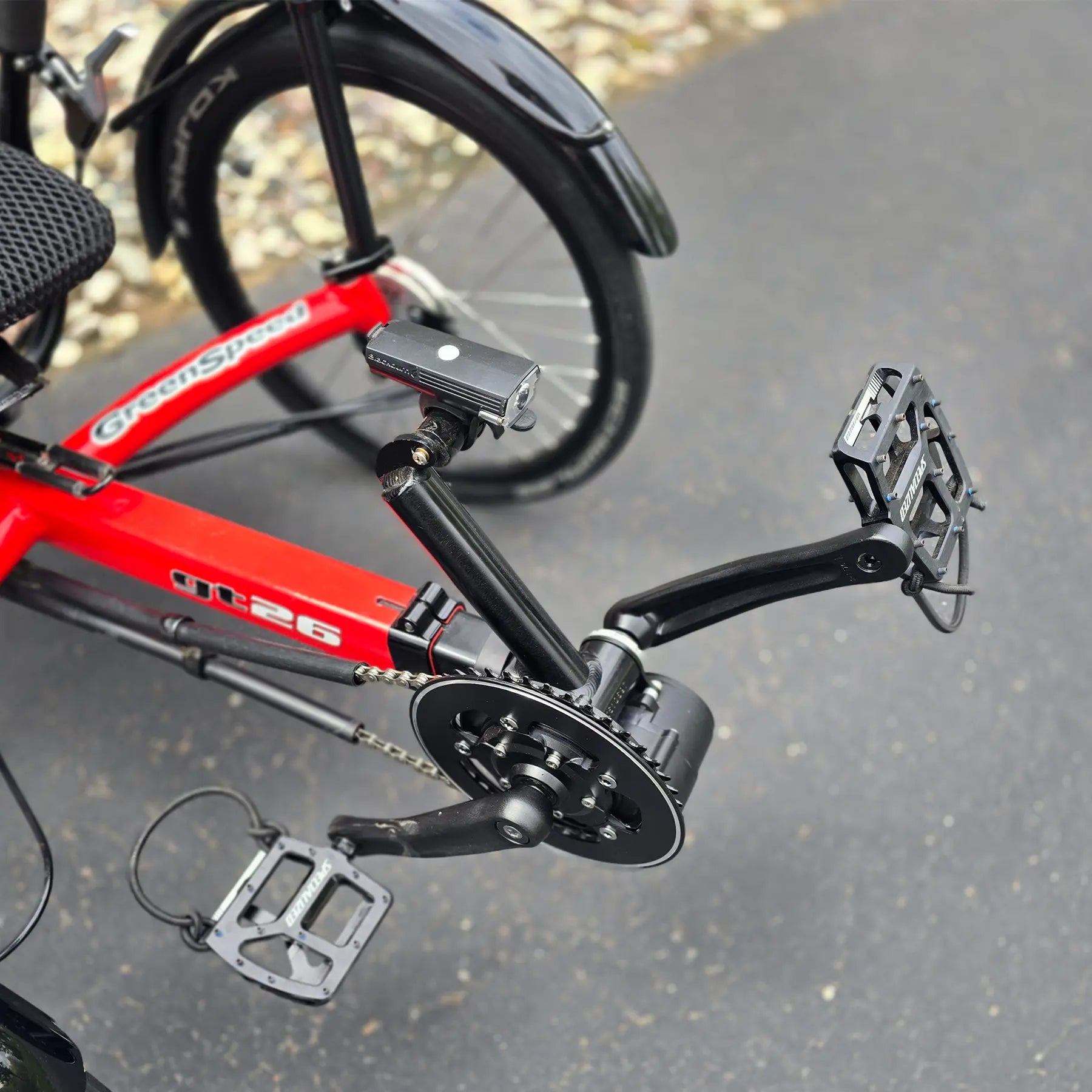 Closeup view of the light mount, headlight, pedals and mid-drive motor on the Greenspeed Used GT26 with E.B.O. e-Assist Red Recumbent Trike in an outdoor setting.