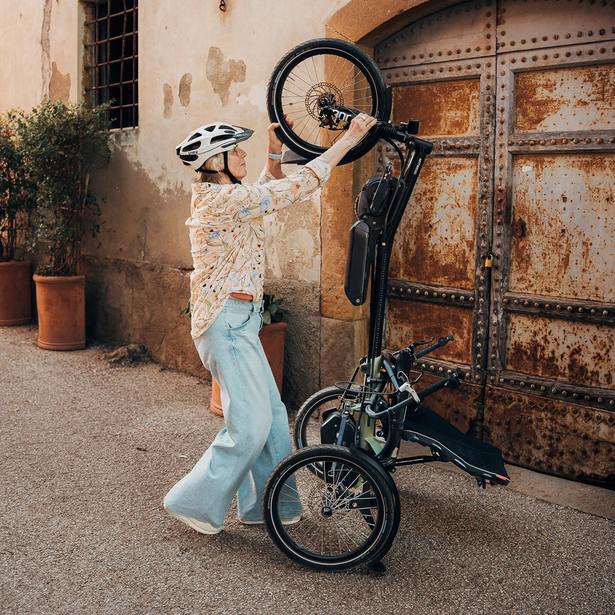 A woman shows how the Hase Kettwiesel One Plus Enviolo Bosch Performance CX Pale Green Recumbent Trike can be stored in an upright position for storage.