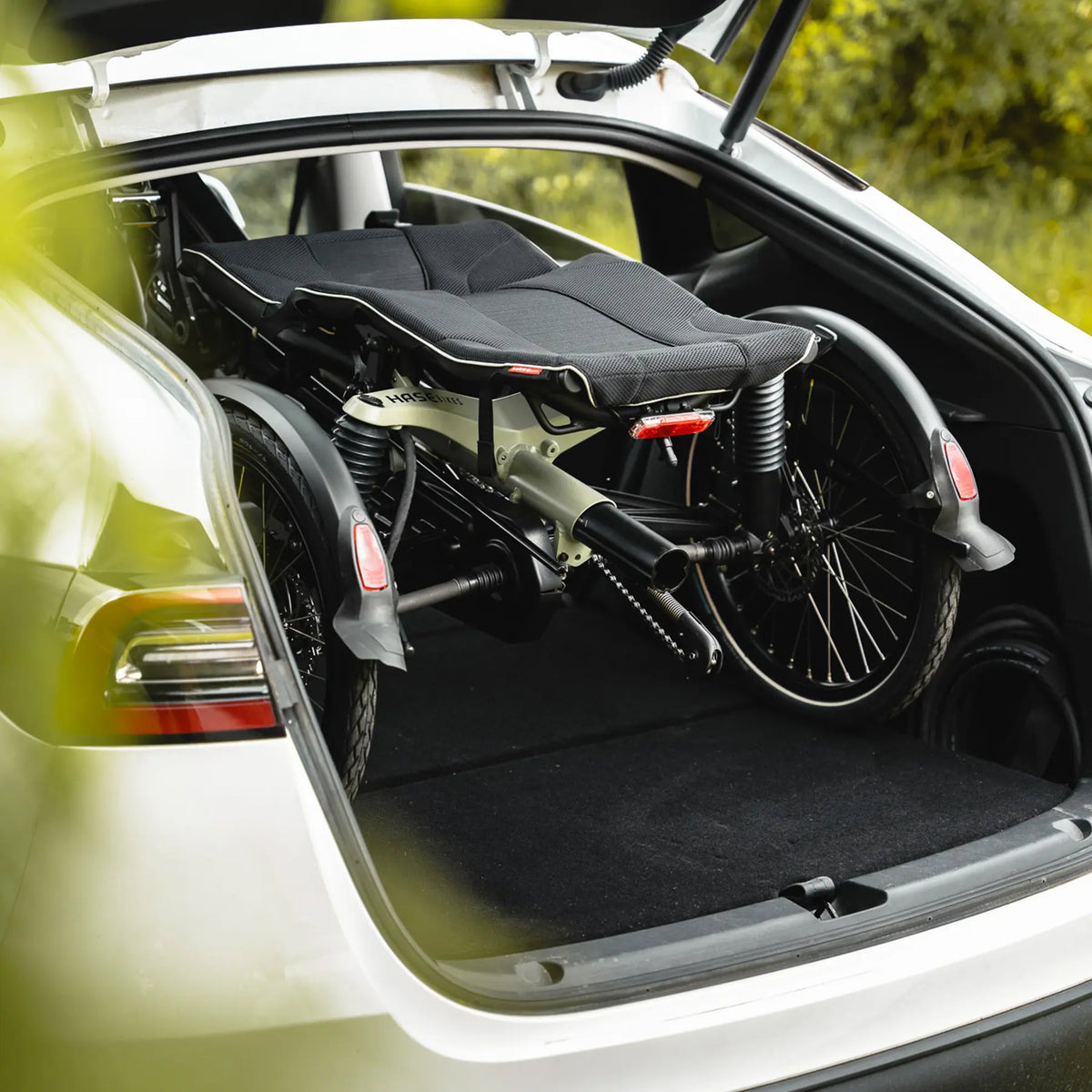 Closeup view of the Hase Kettwiesel One Plus Enviolo Bosch Performance CX Pale Green Recumbent Trike folded in a hatchback car.