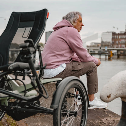 A man views a waterfront setting with  the Hase Kettwiesel One Plus Enviolo Bosch Performance CX Pale Green Recumbent Trike in the background.