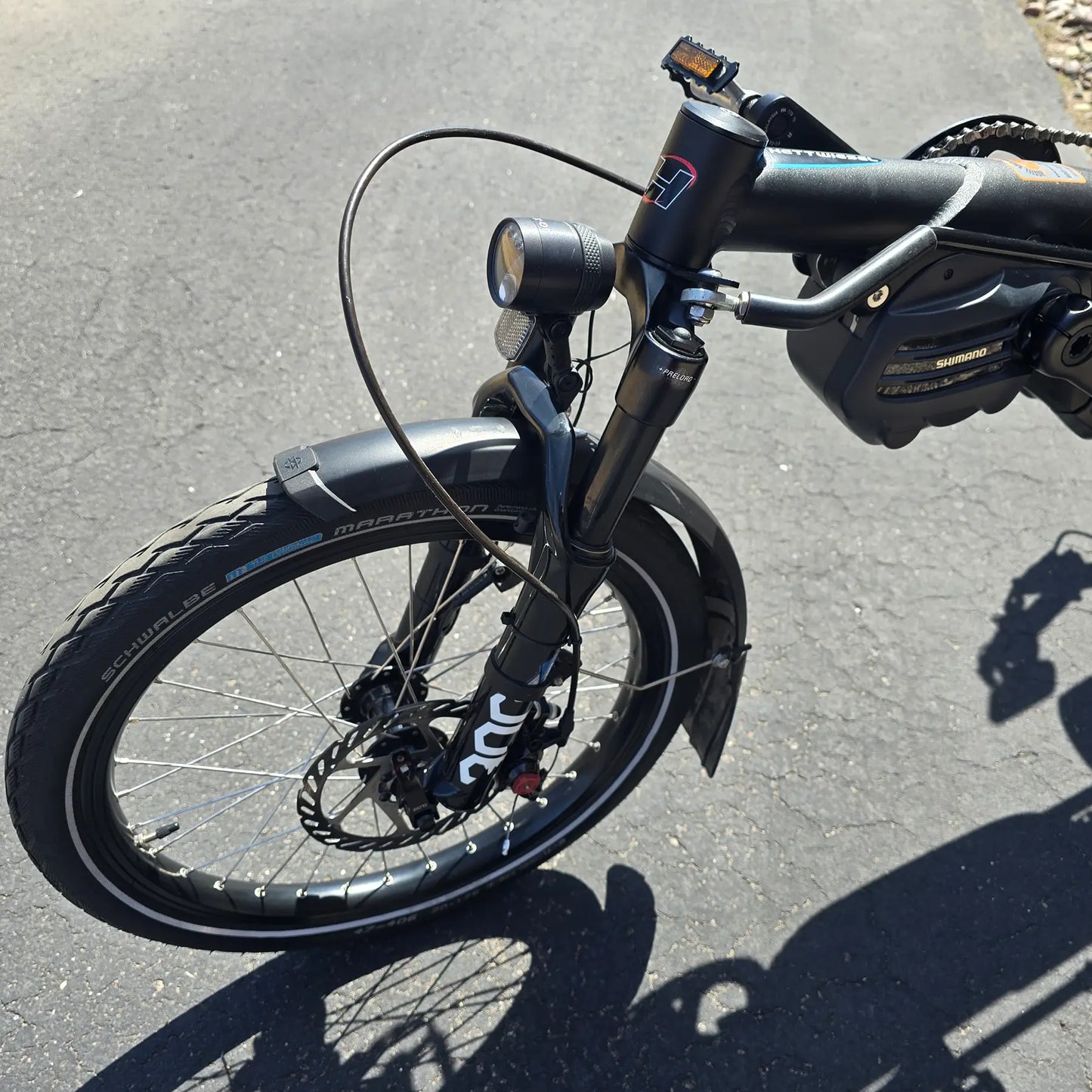 Closeup view of the motor, fork, headlight  and front wheel on the Hase Used 2022 Kettwiesel Evo Steps 6100 with 630wh Battery and 2A Charger Recumbent Trike in an outdoor setting.