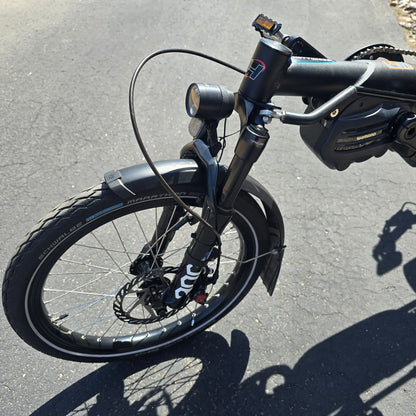 Closeup view of the motor, fork, headlight  and front wheel on the Hase Used 2022 Kettwiesel Evo Steps 6100 with 630wh Battery and 2A Charger Recumbent Trike in an outdoor setting.