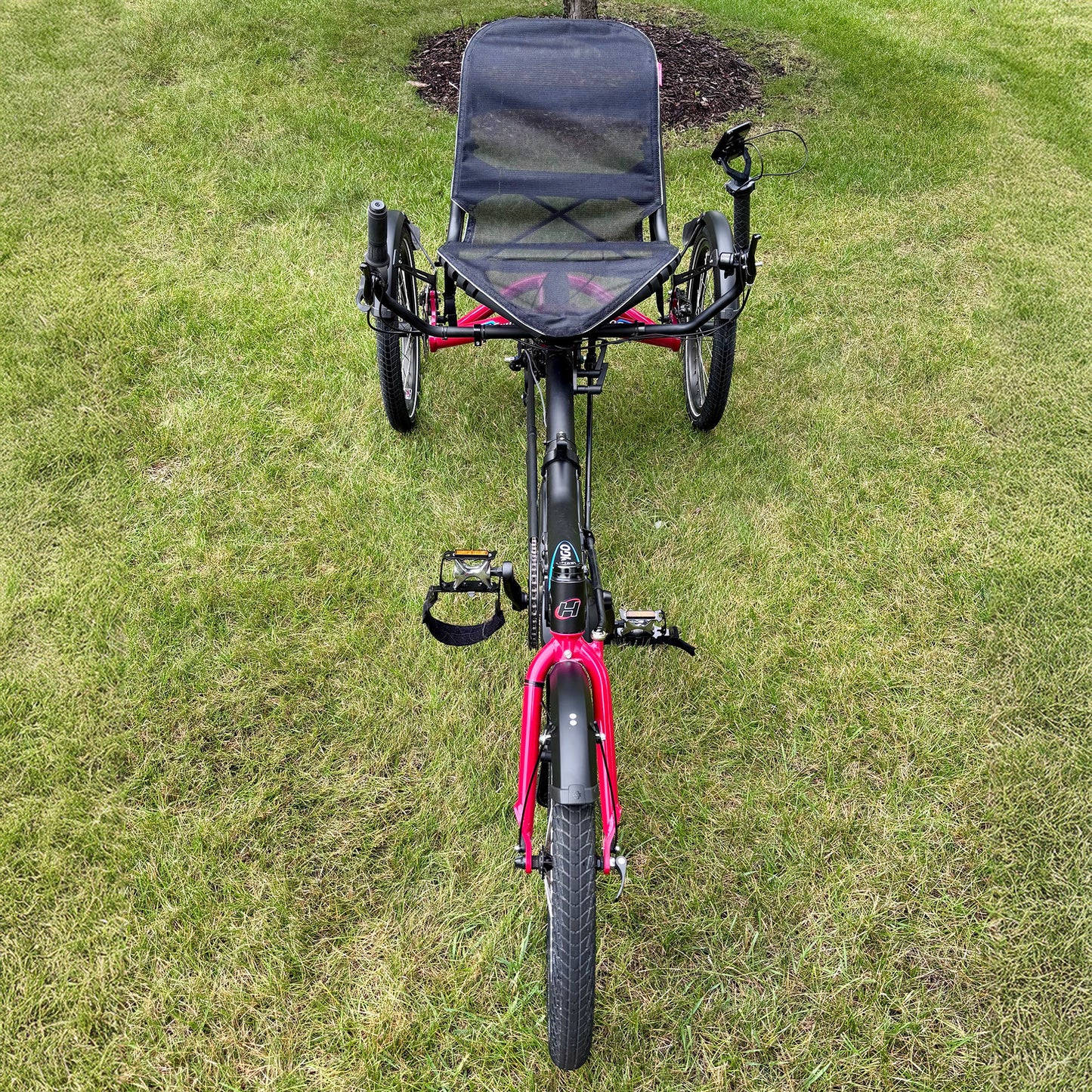 Red recumbent Hase Trigo tricycle on a grassy area.