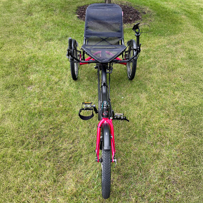 Red recumbent Hase Trigo tricycle on a grassy area.