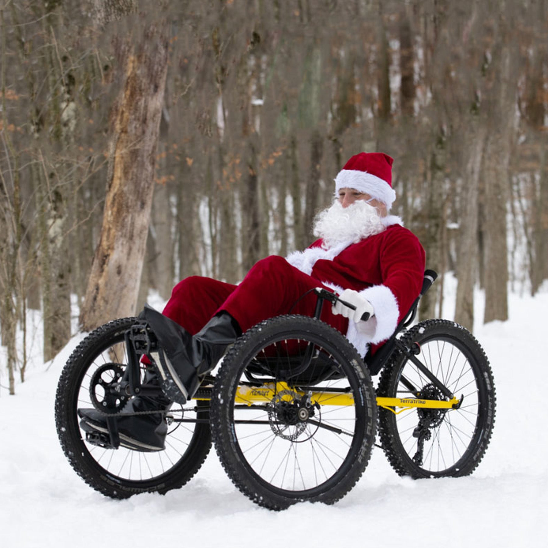Person dressed as Santa Claus riding a recumbent trike in a snowy forest.