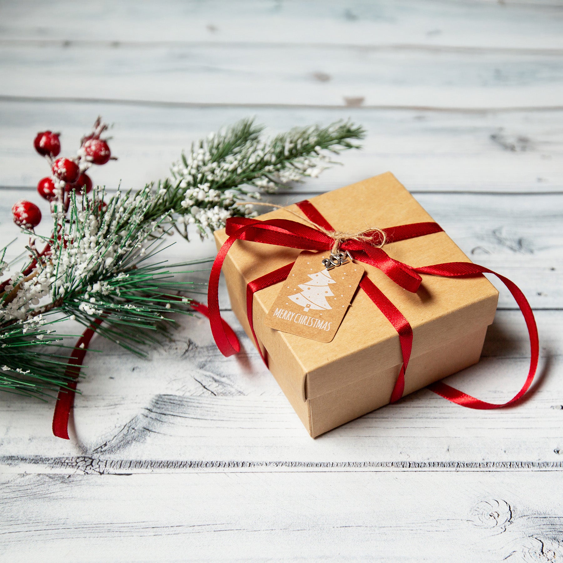 A holiday gift sits next to a spring of greenery and berries against a grey wooden background.