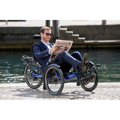 Man sitting on the HP Velotechnik Gekko fx 20 Sport Recumbent Trike in Deep Blue reading a newspaper alongside a river in the city.