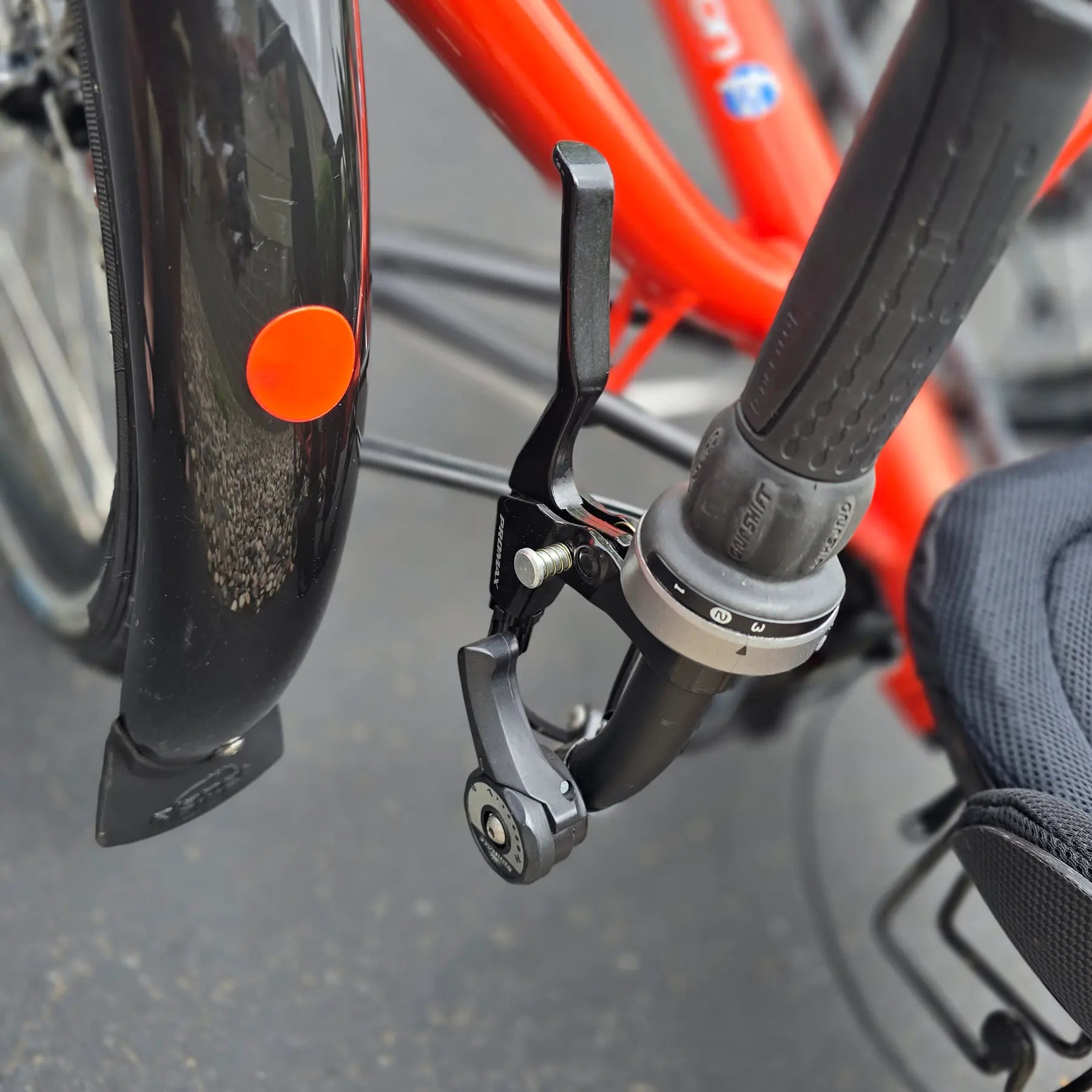 Closeup view of the front shifter and parking brake on the HP Velotechnik Used Scorpion fs 20 Orange Recumbent Trike in an outdoor setting. 