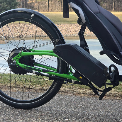 Closeup view of the rear wheel and b ttery on the ICE Adventure HD 26 FS PERS Chainless Kiwi Green Recumbent Trike on a bike path near a melting pond.