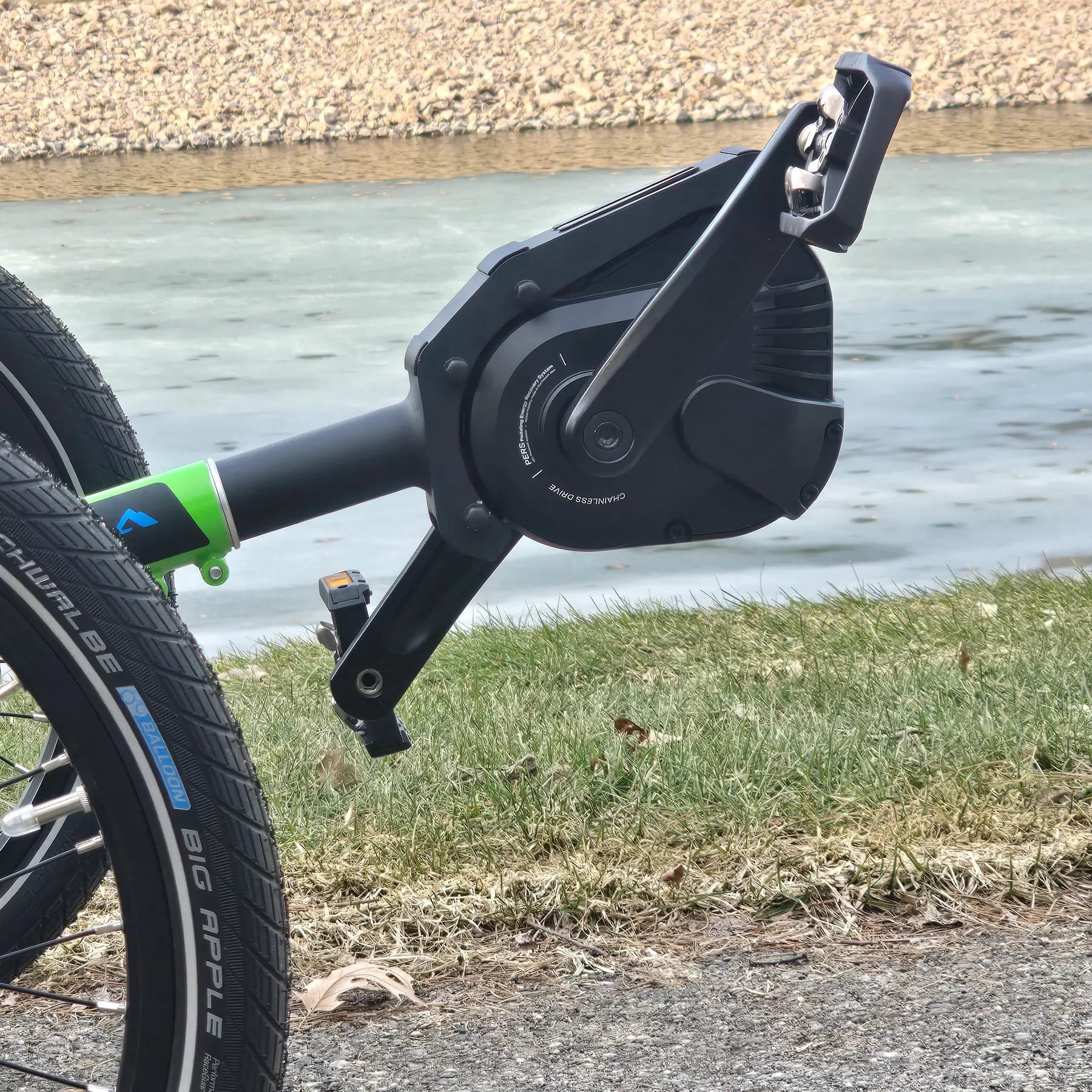 Closeup view of pedals and motor on the ICE Adventure HD 26 FS PERS Chainless Kiwi Green Recumbent Trike on a bike path near a melting pond.