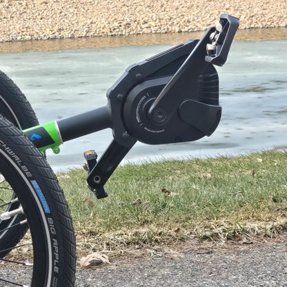 Closeup view of pedals and motor on the ICE Adventure HD 26 FS PERS Chainless Kiwi Green Recumbent Trike on a bike path near a melting pond.