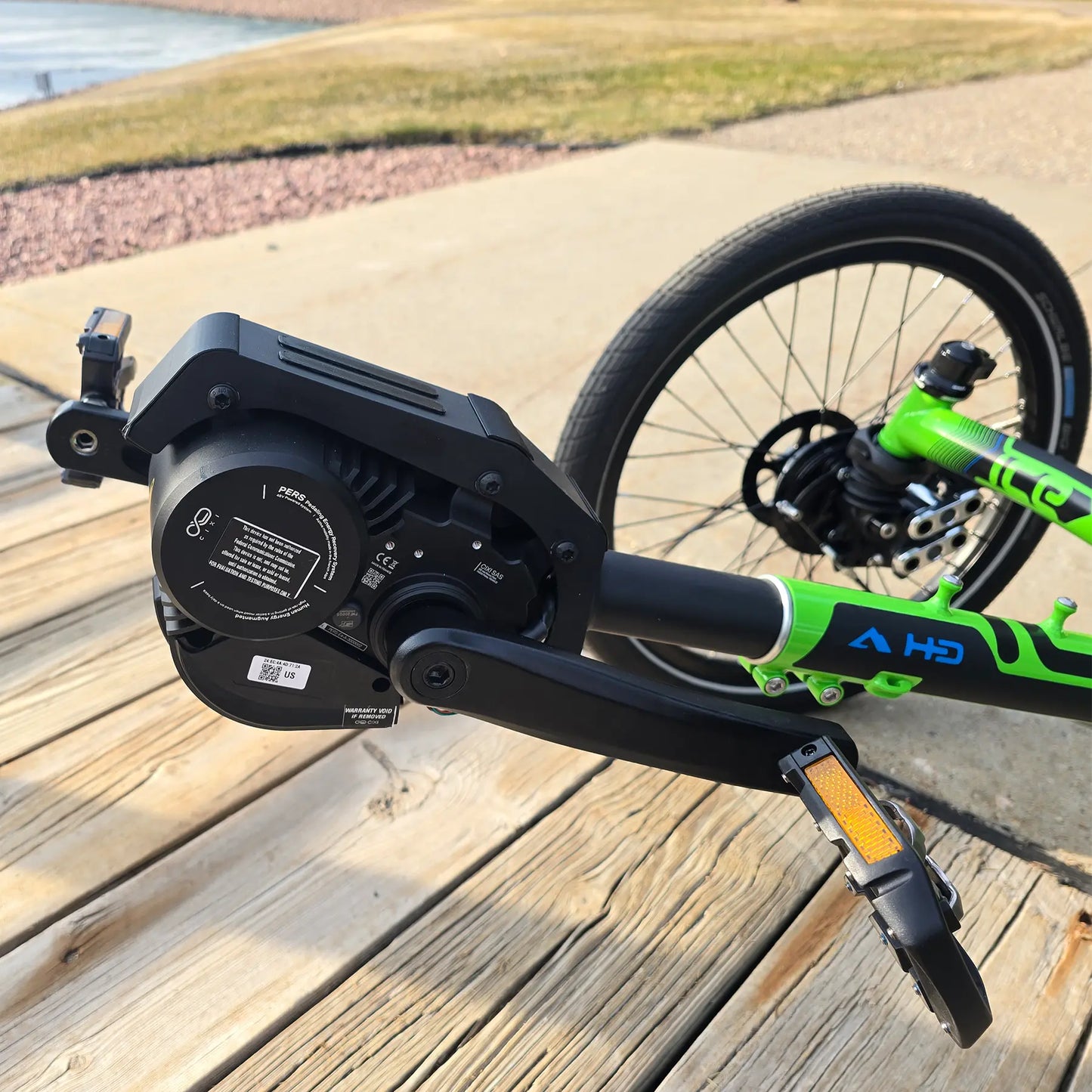 Closeup view of pedals and motor on the ICE Adventure HD 26 FS PERS Chainless Kiwi Green Recumbent Trike on a bike path near a melting pond.