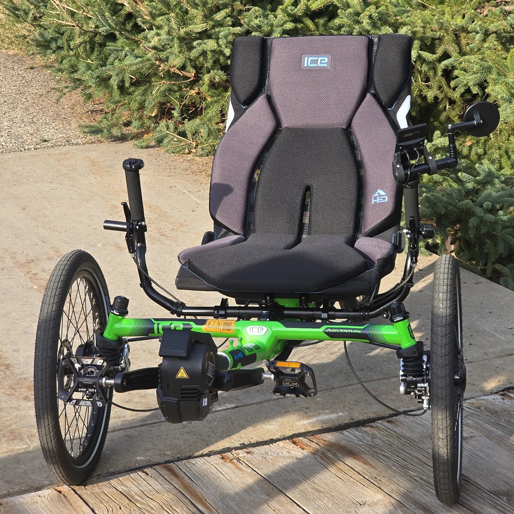 Front view of the ICE Adventure HD 26 FS PERS Chainless Kiwi Green Recumbent Trike on a bike path by a pine tree.