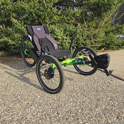 Angled view of the ICE Adventure HD 26 FS PERS Chainless Kiwi Green Recumbent Trike on a bike path near a pine tree.